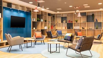 Un espace de détente moderne, doté de sièges confortables, d’un téléviseur à écran plat et d’étagères en bois où sont exposés divers objets décoratifs.