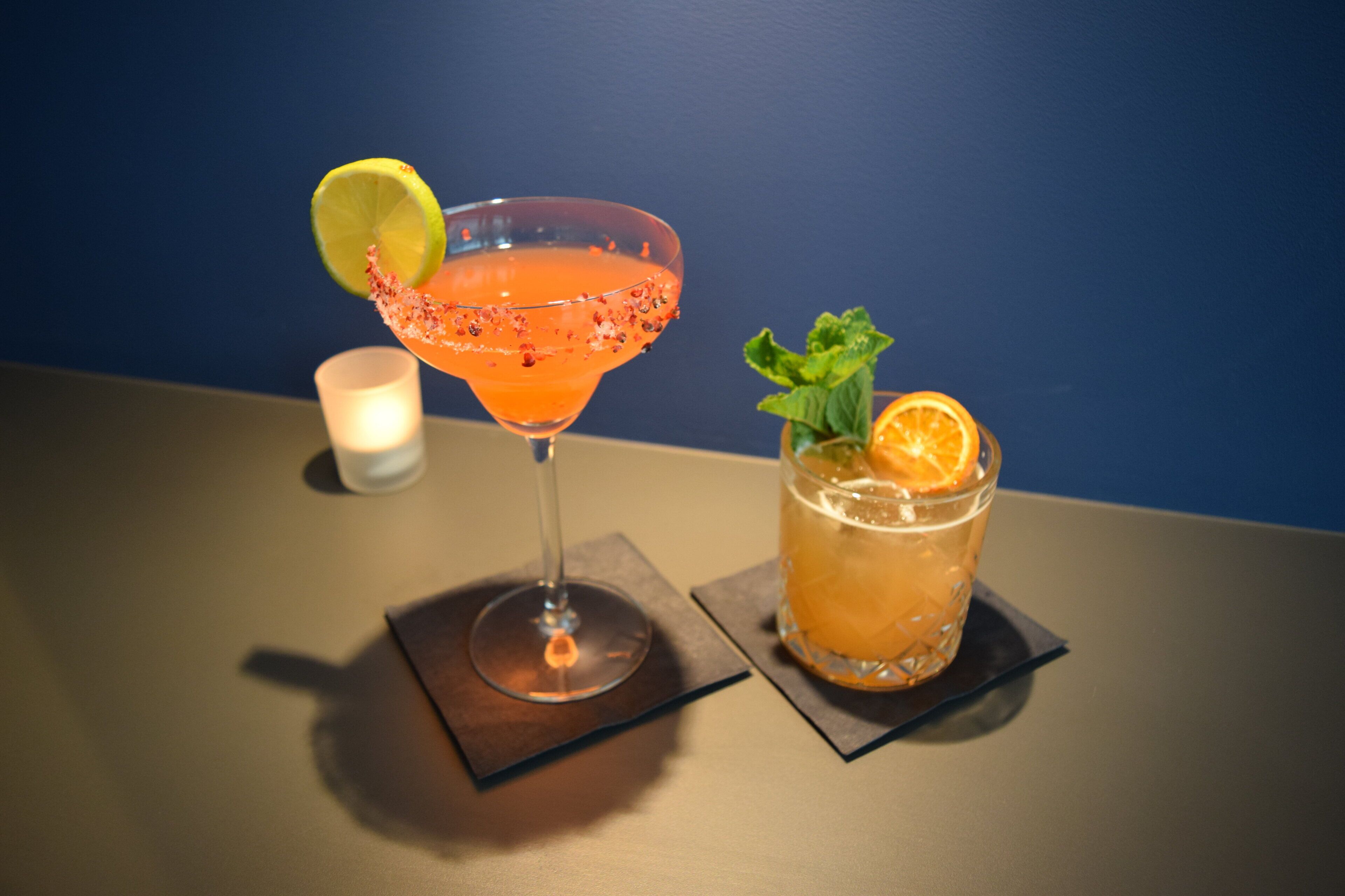 Two drinks on a table with a candle in the background.