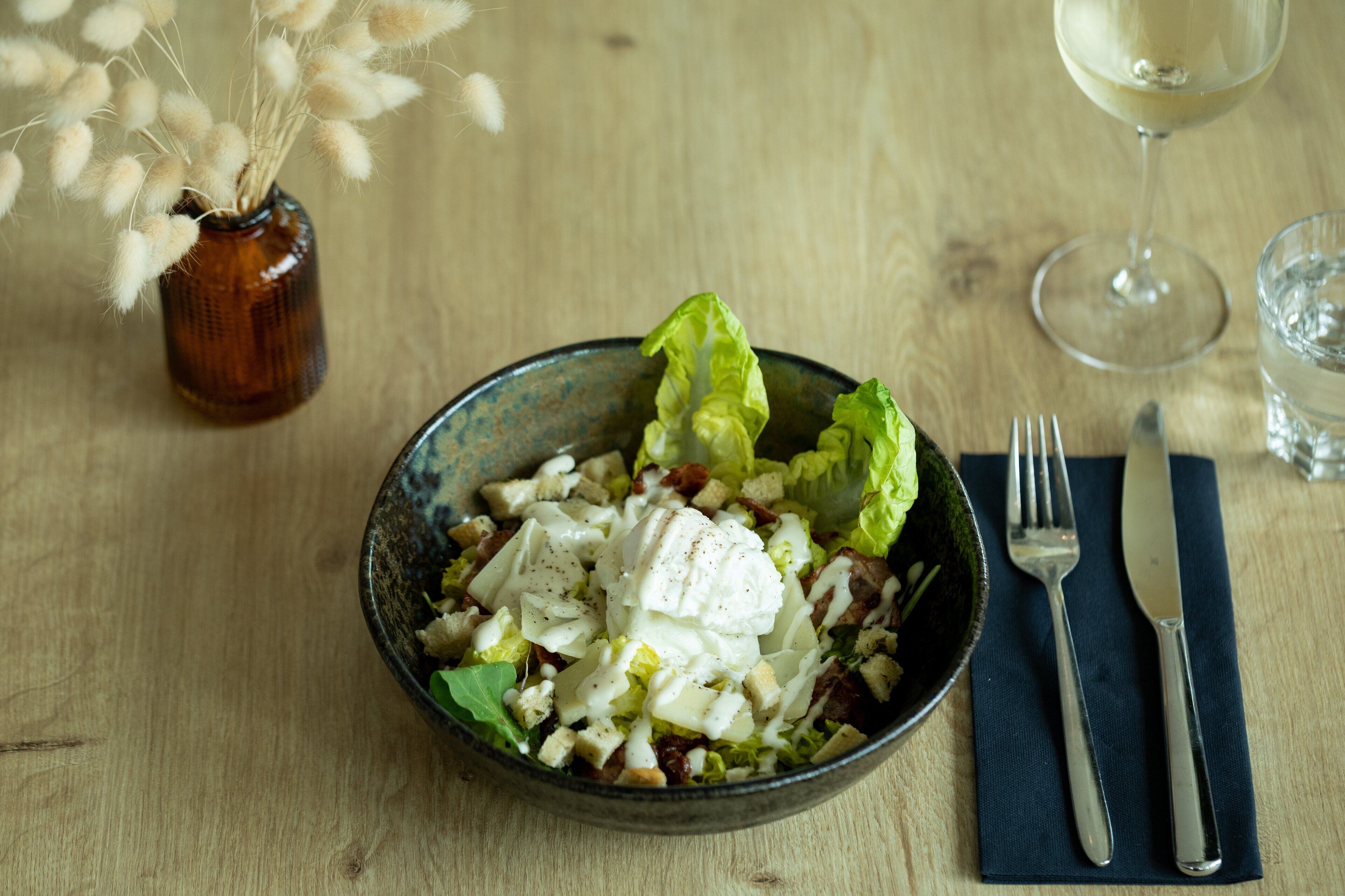 A bowl of salad with croutons, lettuce, and a creamy dressing on a wooden table.