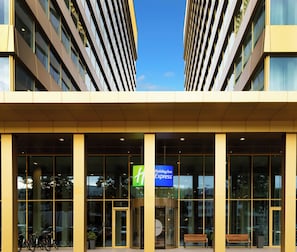 A Holiday Inn Express building with a glass facade, a central entrance with a revolving door, and a sign above the entrance. - Holiday Inn Express Amsterdam - North Riverside by IHG (Amsterdam)