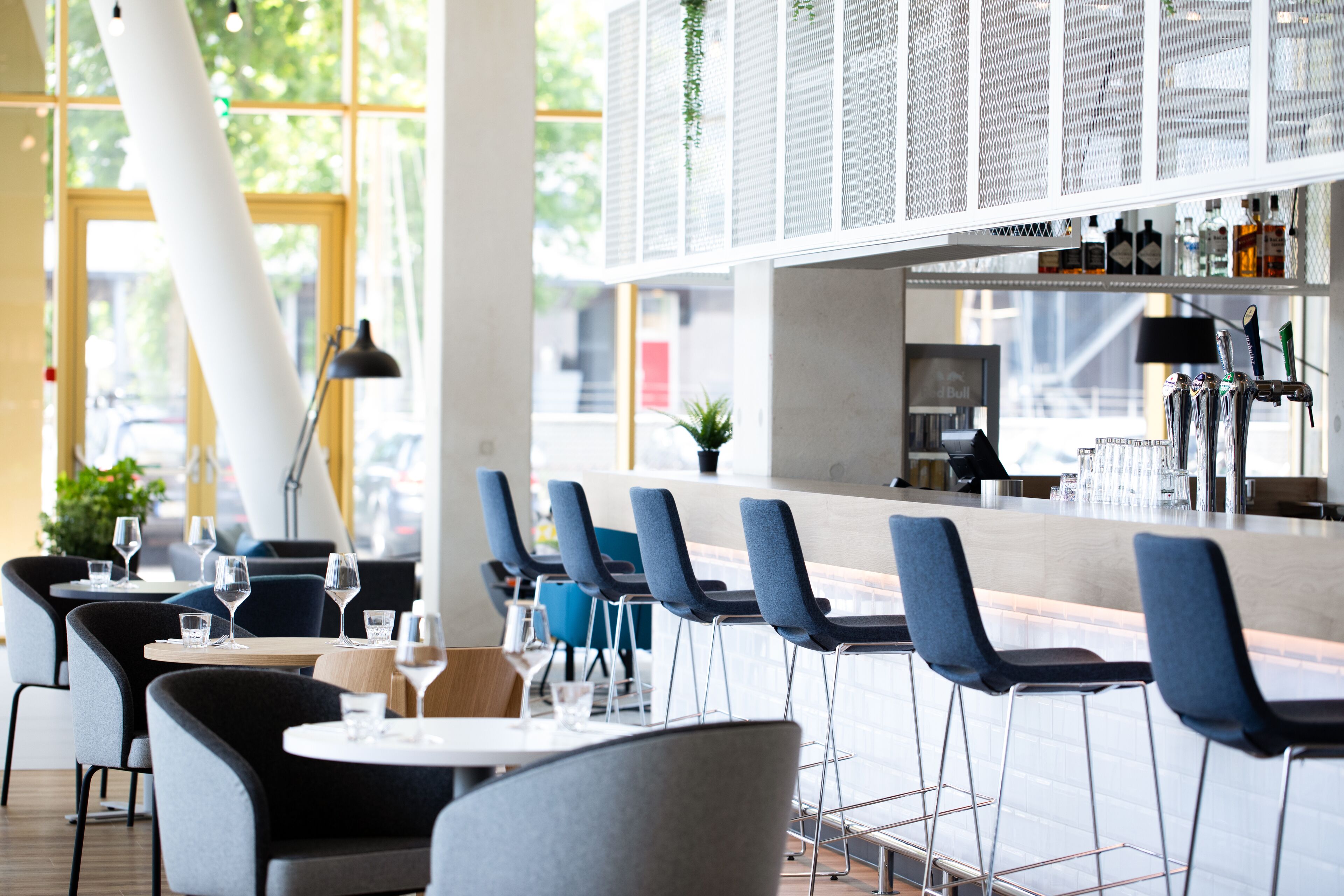 Un área de bar moderna con una barra larga, taburetes azules y una variedad de botellas y vasos.