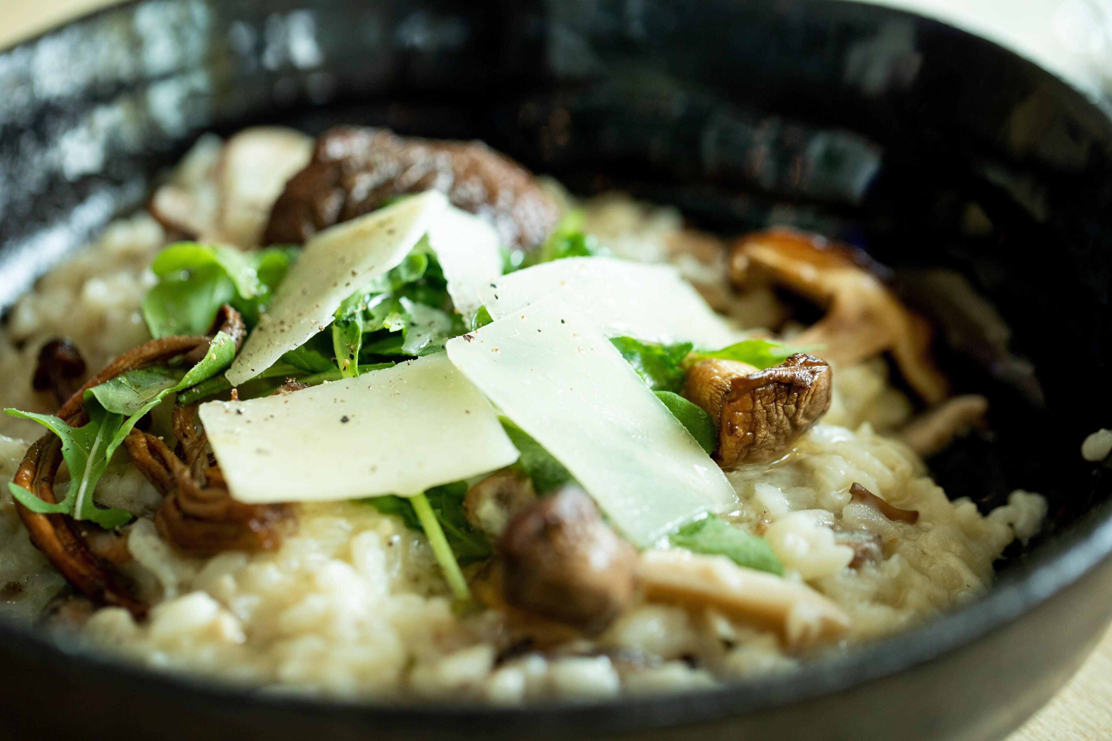 A bowl of creamy risotto with mushrooms, cheese, and greens.