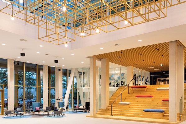 A spacious lobby with a modern staircase, large windows, and a geometric ceiling design.