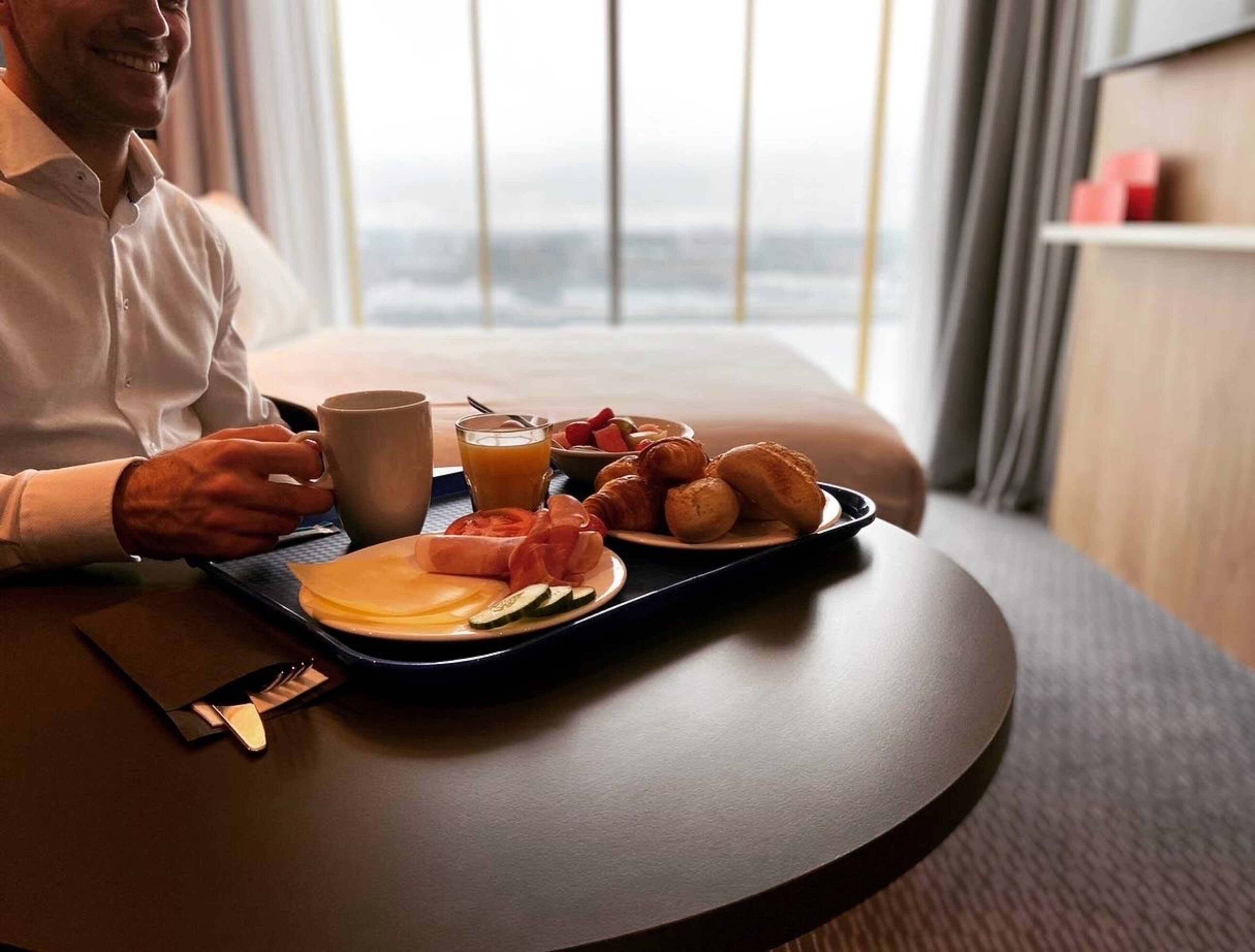 Une chambre d’hôtel avec un plateau de petit-déjeuner sur une table ronde, une fenêtre donnant sur un beau paysage et une table de chevet avec une lampe.