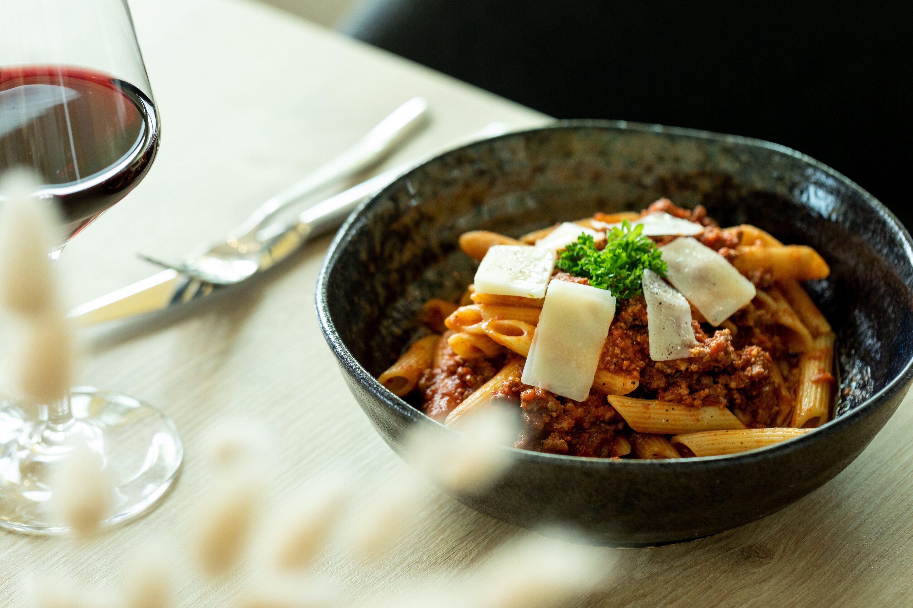 A bowl of pasta with meat sauce and cheese on a table.