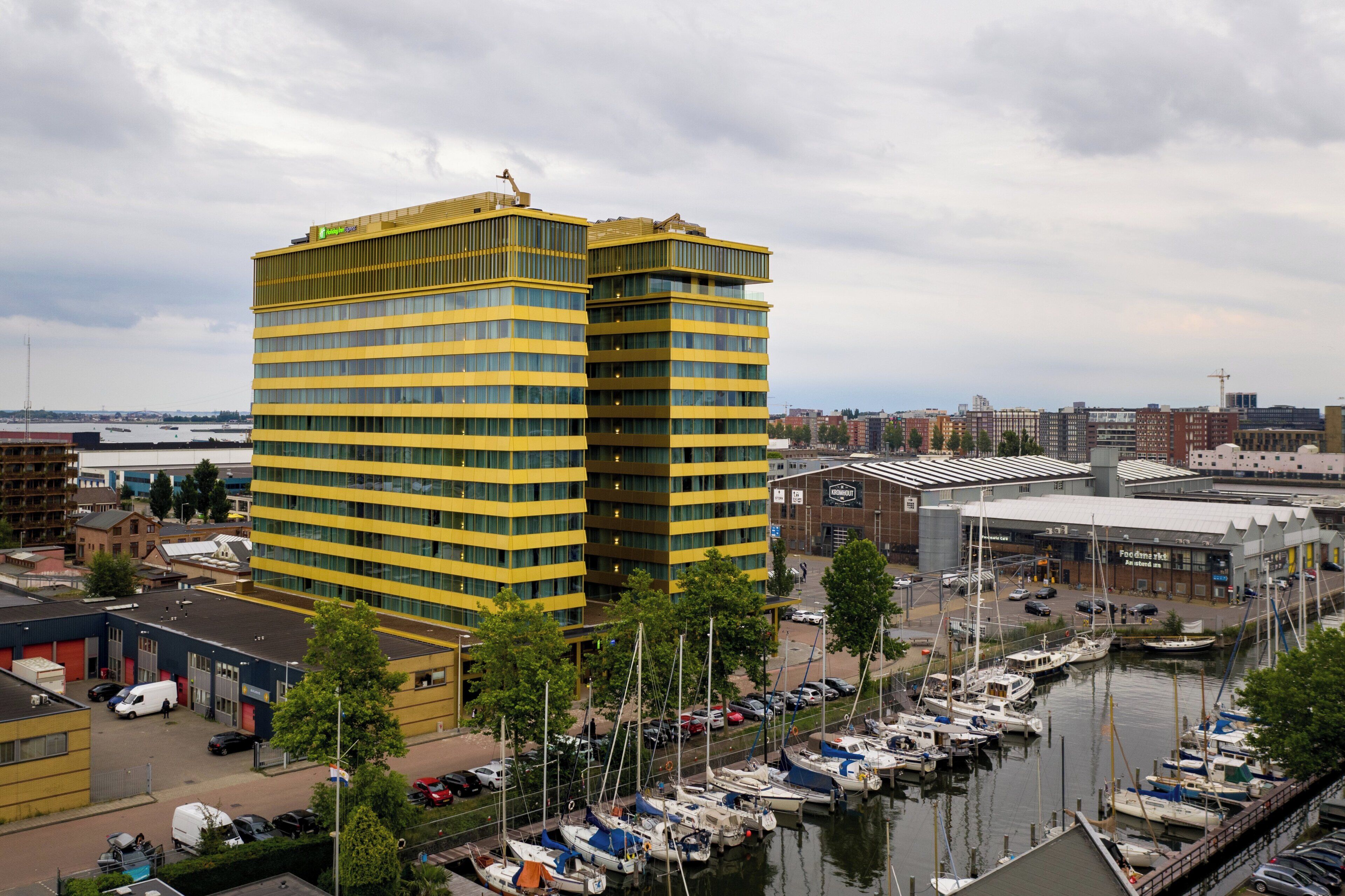 A high-rise building with a yellow facade, a marina with boats, and a cityscape in the background.