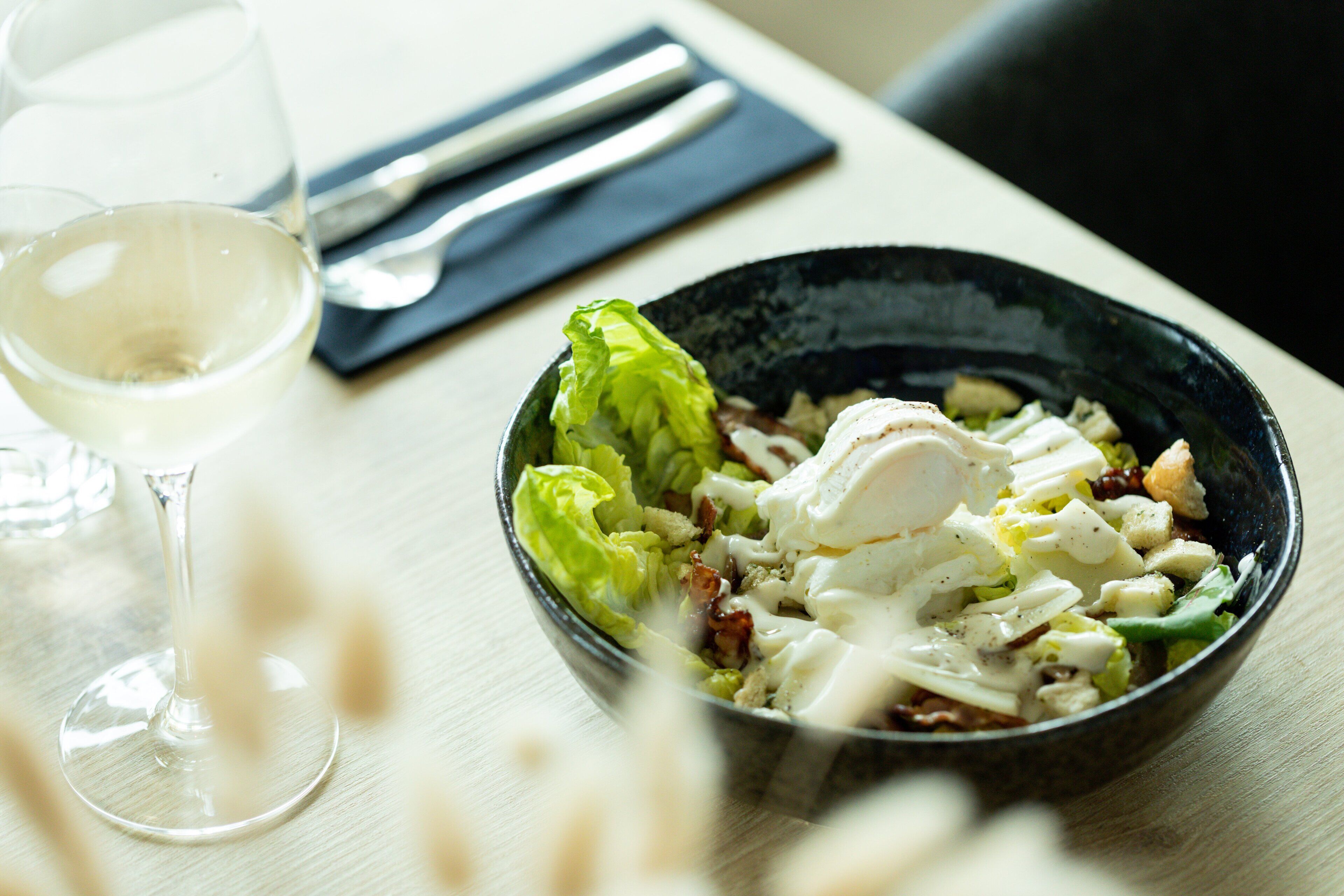 A bowl of salad with a fork and knife on a napkin beside it.