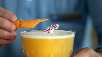 A cocktail in a glass with a decorative garnish, held by a person.