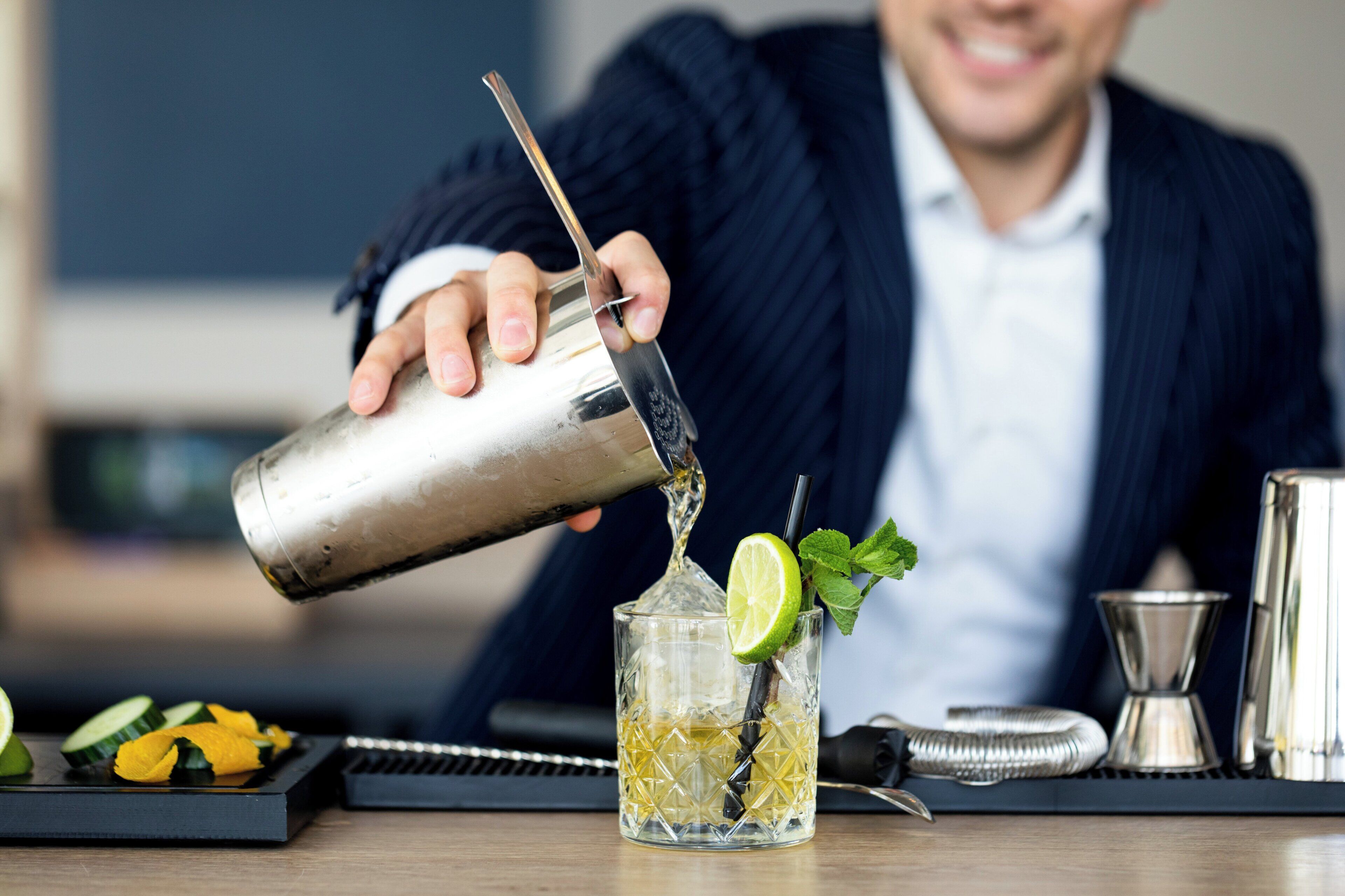 A person pouring a drink into a glass with a lime wedge and mint leaves.