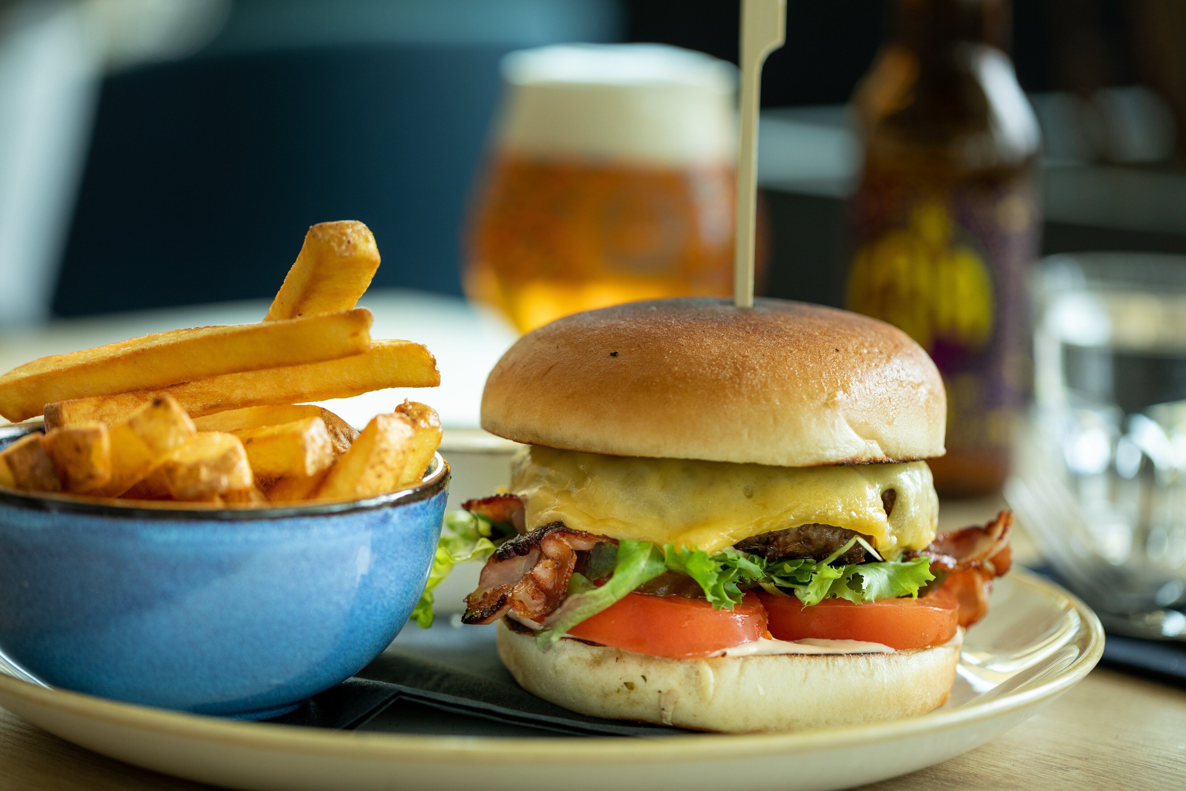 A meal consisting of a burger with lettuce, tomato, and bacon, and a bowl of French fries.