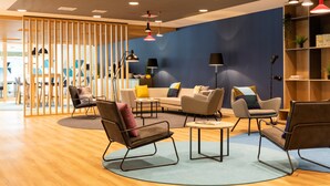 A modern lounge area with a wooden floor, a blue accent wall, and a variety of seating options including sofas and chairs. - Holiday Inn Express Amsterdam - North Riverside by IHG (Amsterdam)