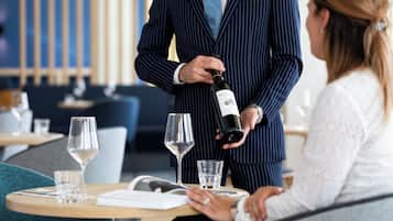 Un hombre con traje a rayas sirve vino en una copa, sentado a la mesa con una mujer.