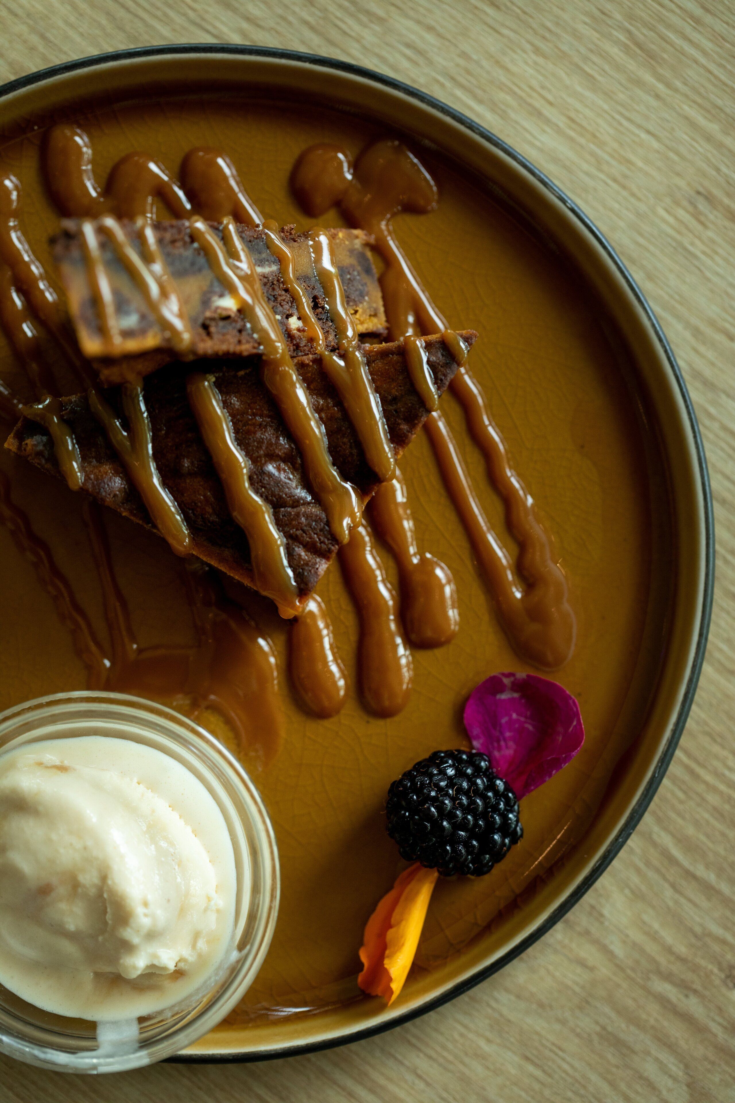 A dessert plate with caramel sauce, a scoop of ice cream, and a blackberry.