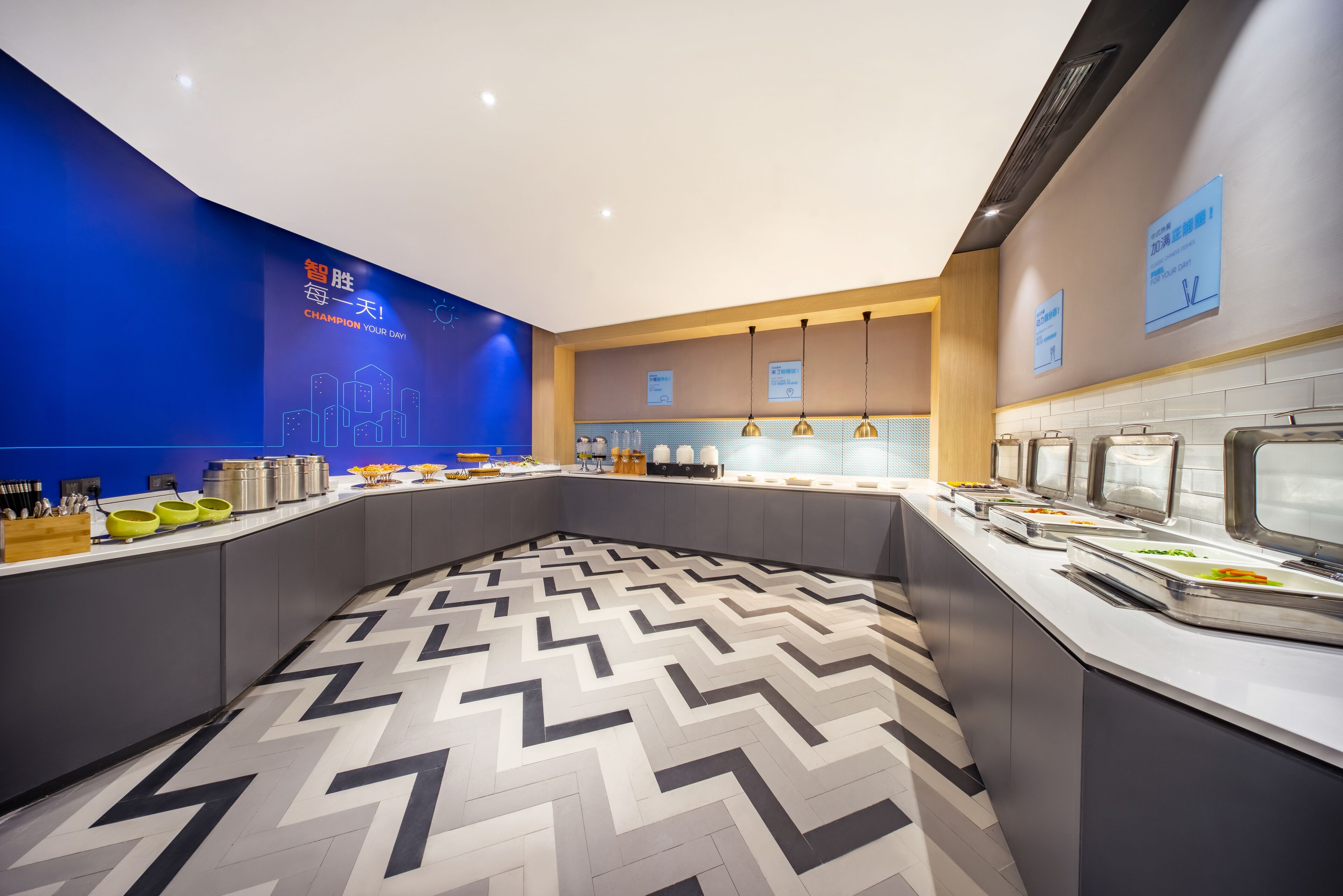 A modern breakfast area with a zigzag patterned floor, a blue wall with motivational text, and buffet counters with food items.