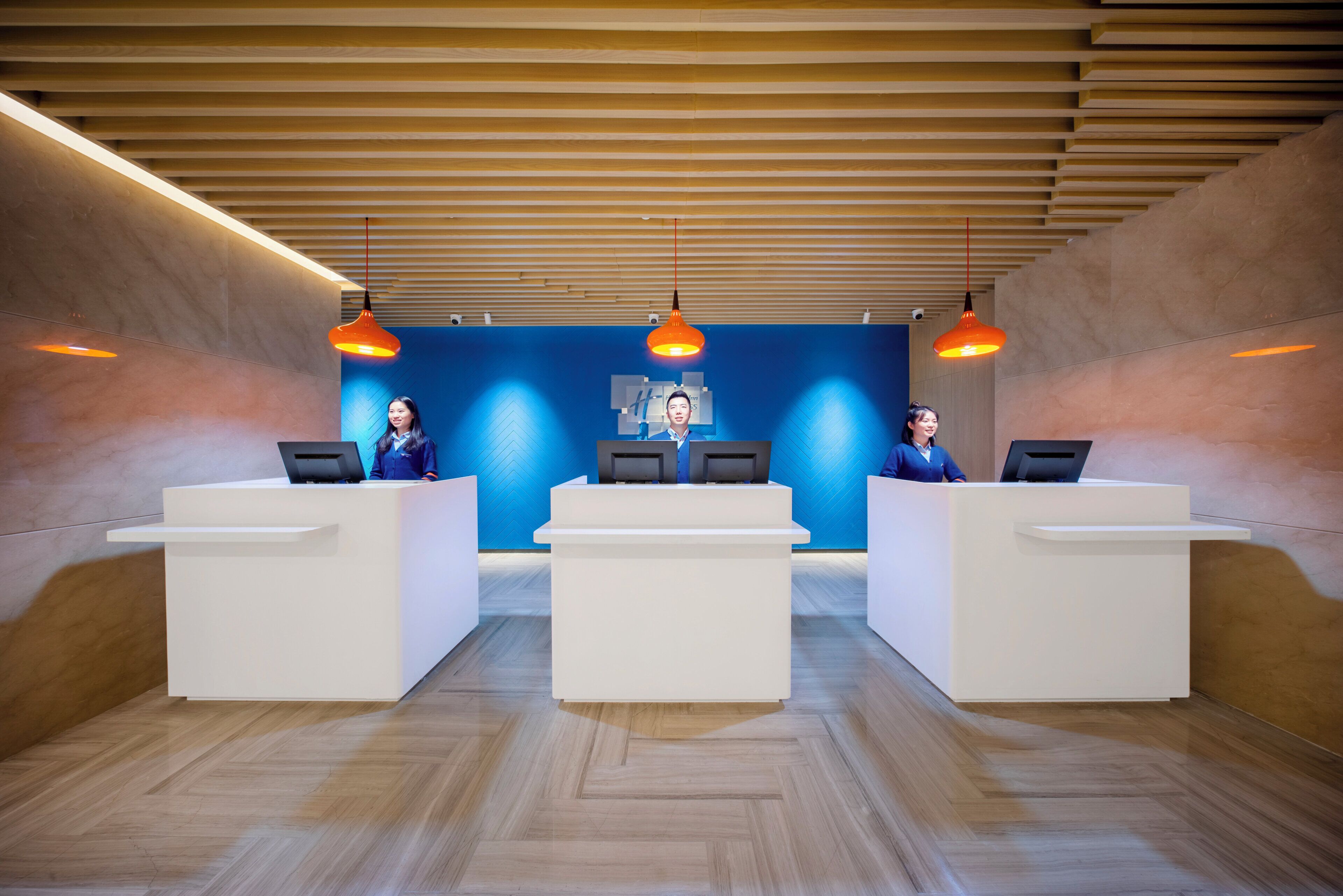 Un área de recepción con tres mostradores blancos, una pared azul con diseño en espiga y techo de listones de madera.