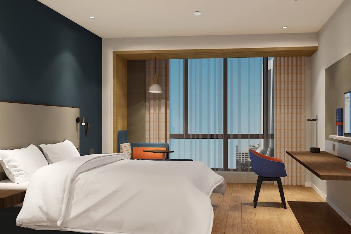 A modern hotel room with a large bed, a desk with a chair, a television, and a large window with curtains.
