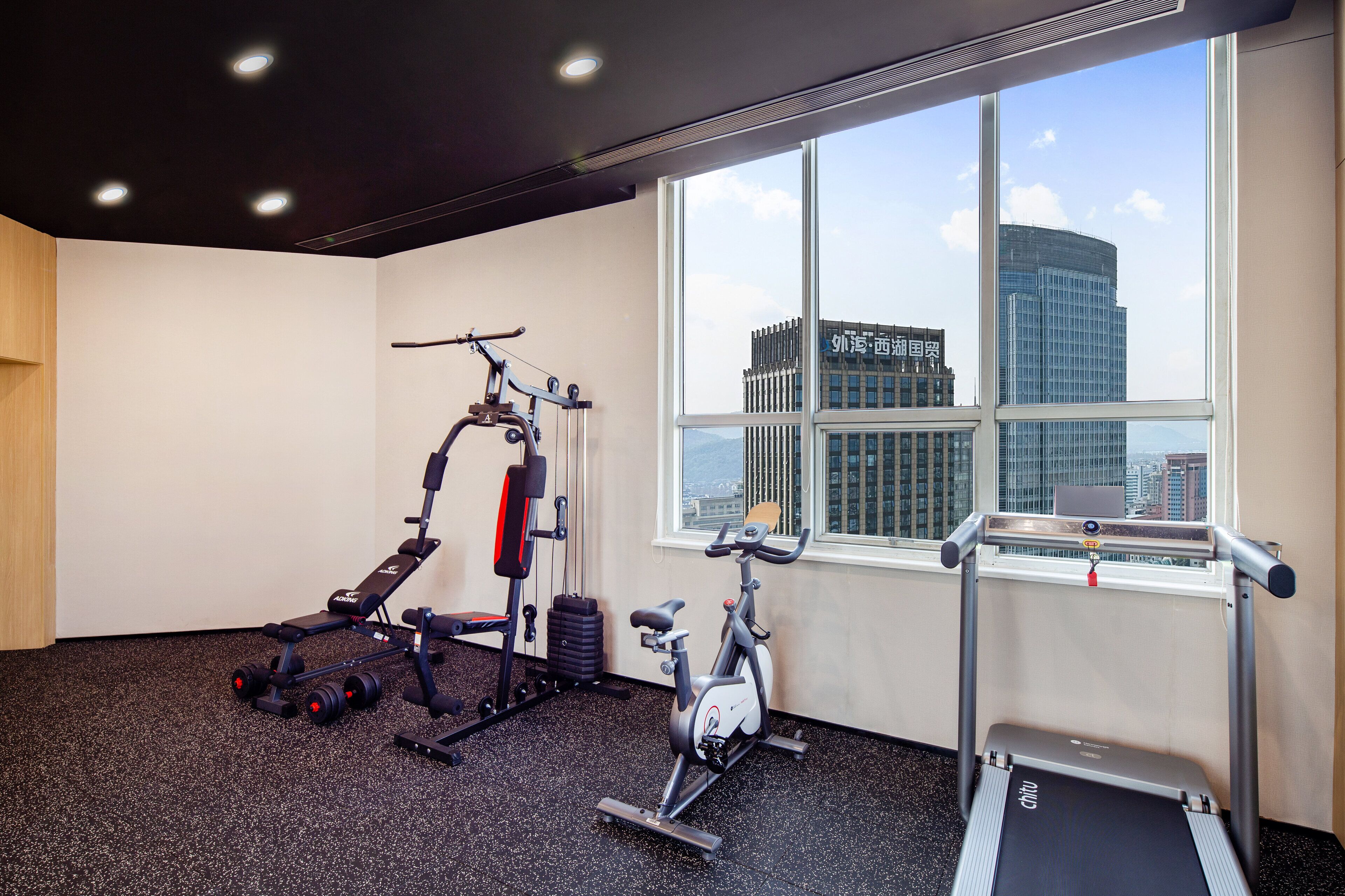 A gym with exercise equipment, a treadmill, and a window with a city view.