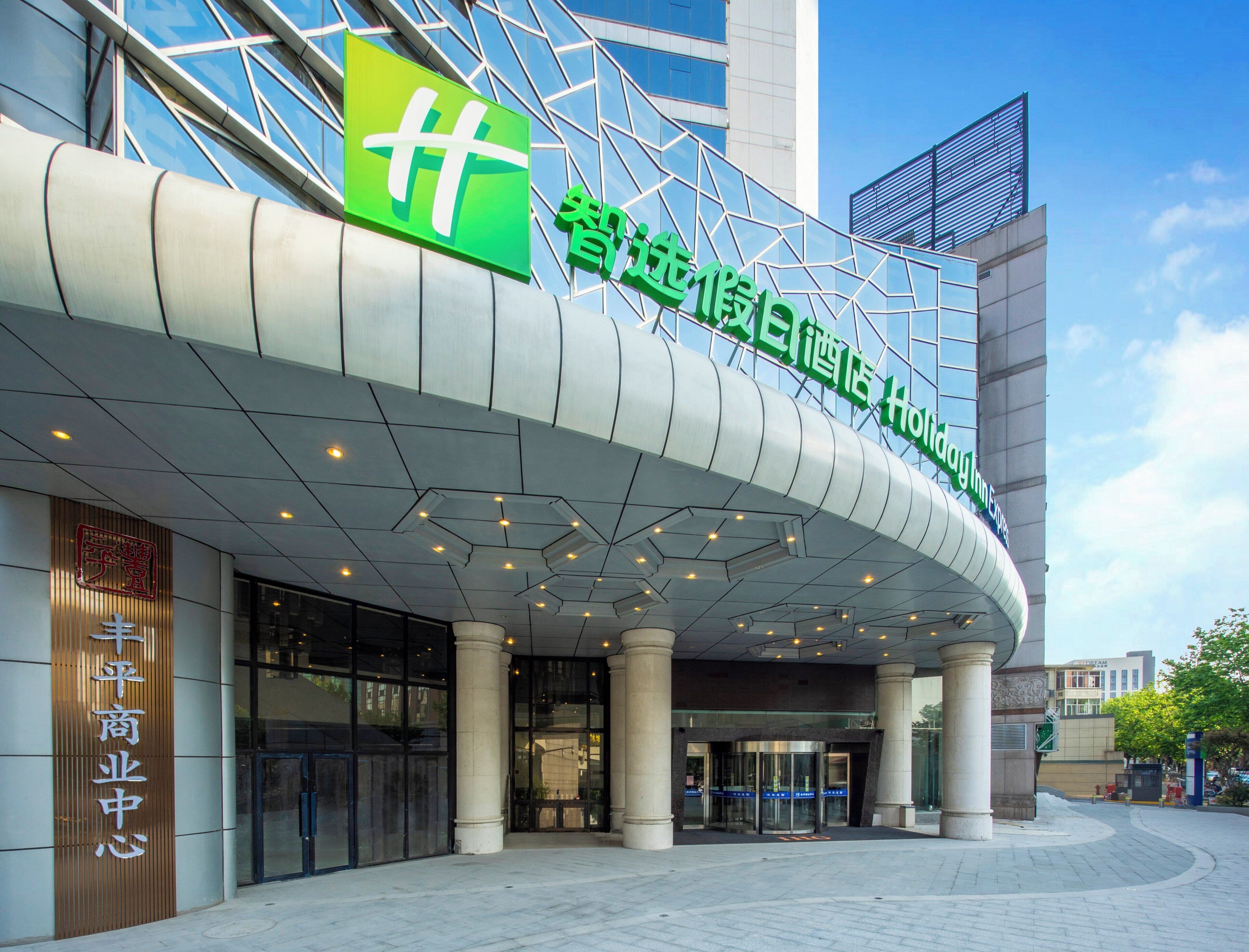 A hotel entrance with a modern design, featuring a prominent green sign with white characters, a curved overhang, and a glass facade.