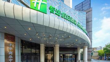 A hotel entrance with a modern design, featuring a prominent green sign with white characters, a curved overhang, and a glass facade.