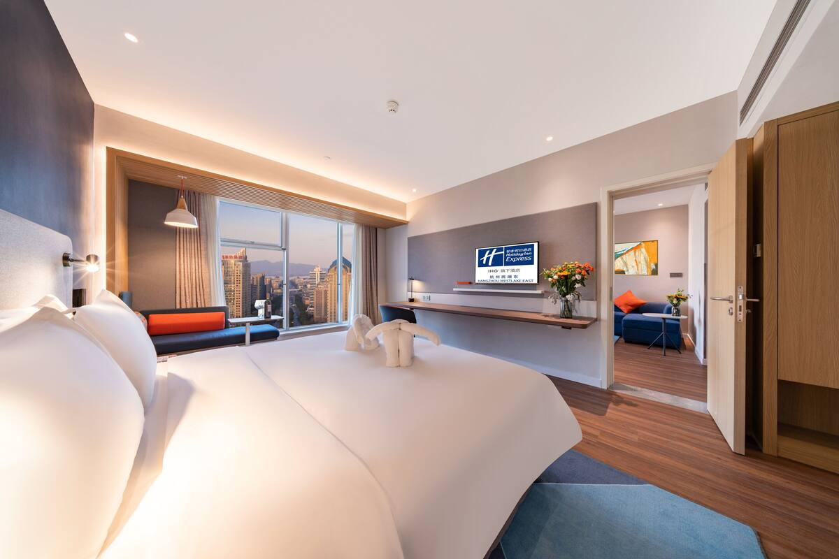 A modern hotel room with a large bed, a city view, a TV, and a desk area.