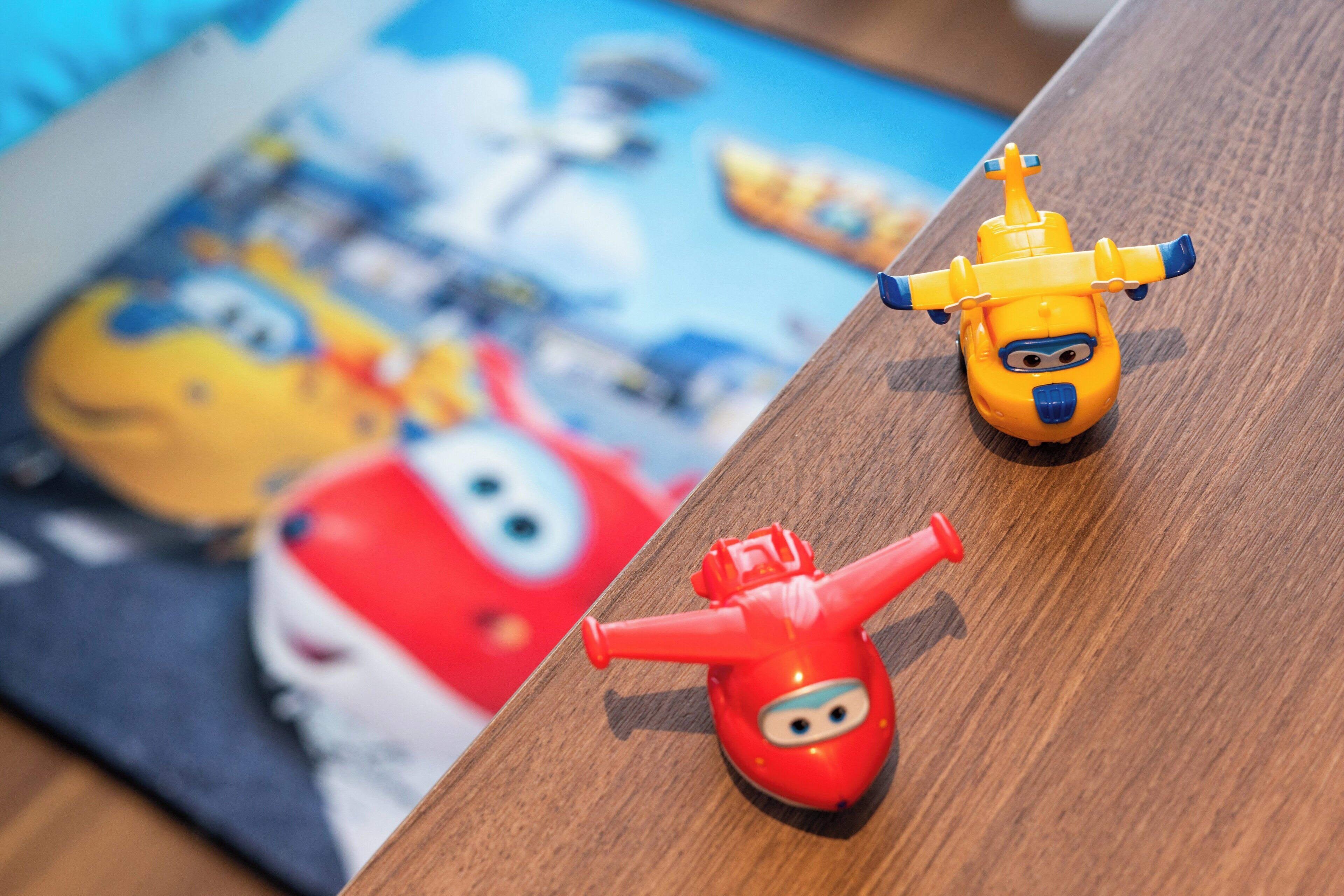 A wooden table with two toy vehicles and a blurred background.