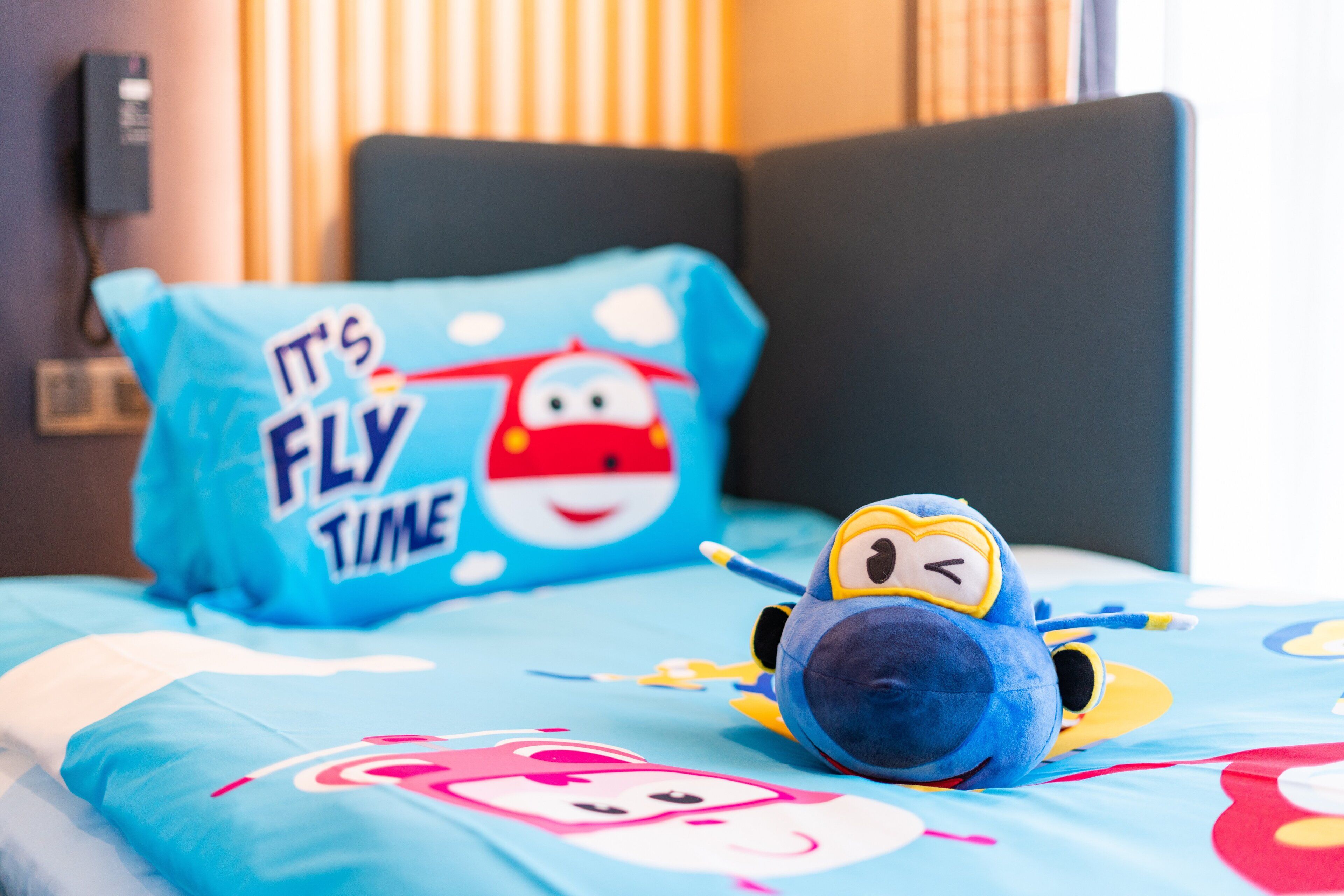 Una cama con un almohadón azul que muestra un personaje de caricatura y el texto 'It's Fly Time'.