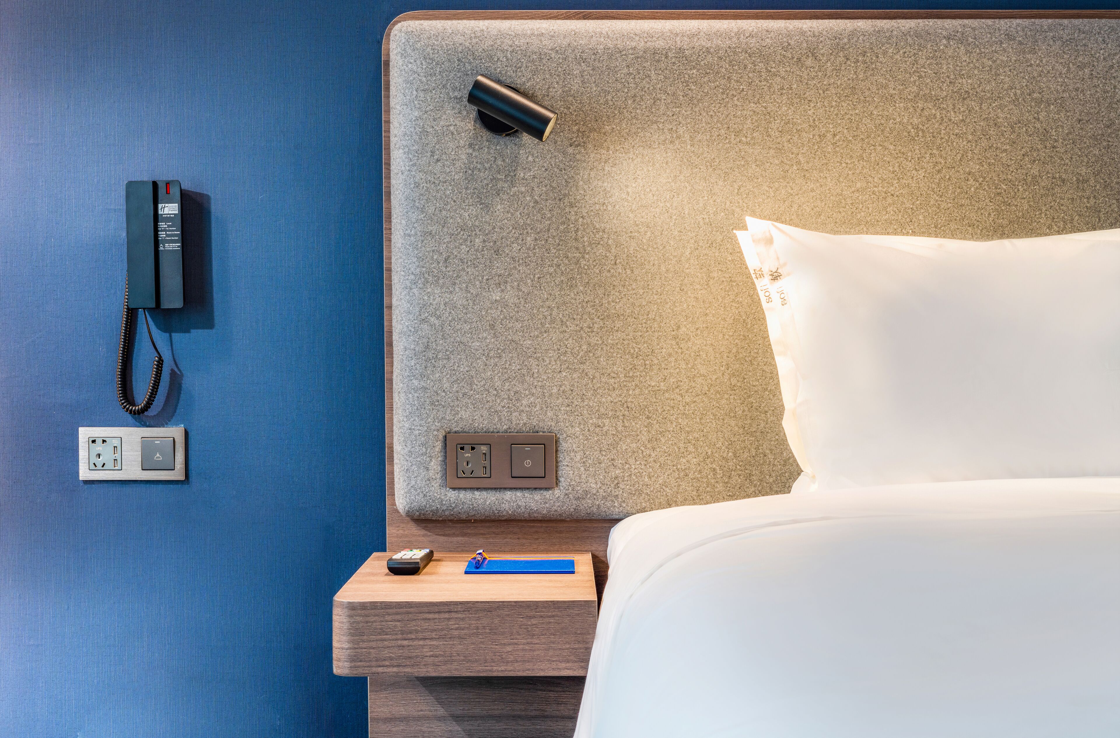 A hotel room with a bed, a nightstand, a phone, and a wall socket.