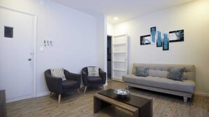 Un saló modern amb un sofà gris, dues butaques, una taula de centre i una estanteria.