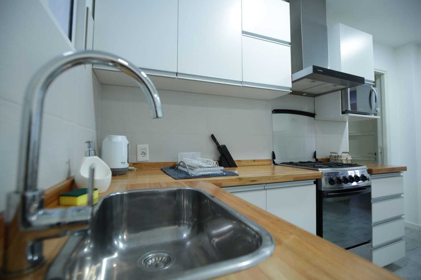 Una cucina moderna con mobili bianchi, un lavello in acciaio inossidabile, un fornello a gas e un microonde.