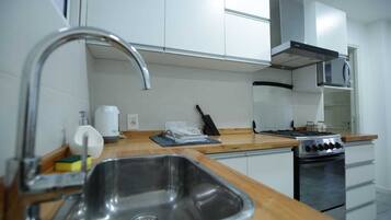 Una cucina moderna con mobili bianchi, un lavello in acciaio inossidabile, un fornello a gas e un microonde.
