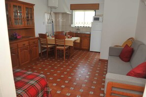 A compact kitchen with wooden cabinets, a dining table with chairs, a grey sofa with red cushions, and a patterned floor. - Turcongel Apartamentos Turisticos (Castro Marim)