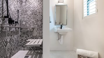 A bathroom with a shower, a sink, a mirror, and a window.