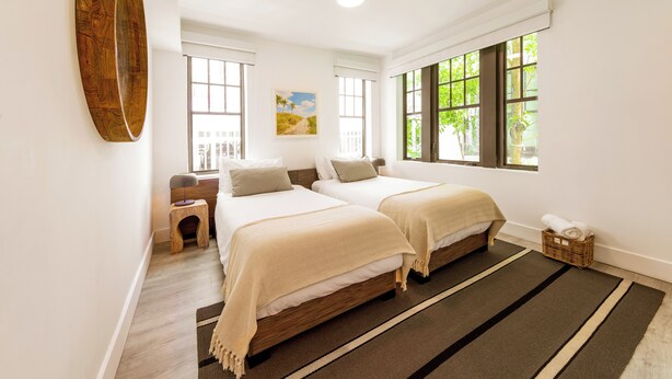 A bedroom with two beds, a wooden floor, a large window, and a painting on the wall.
