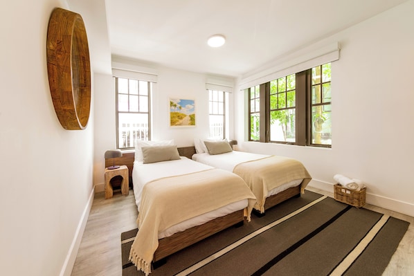 A bedroom with two beds, a wooden floor, a large window, and a painting on the wall. - Casa Sofi (Miami Beach)