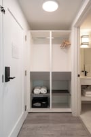 Habitación de hotel con vestidor, una cama y toallas ordenadas, además de un dispositivo electrónico negro sobre una repisa.