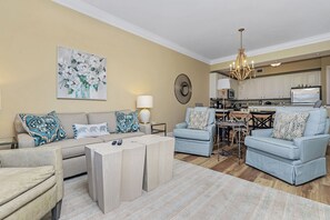 Uma sala de estar com sofá, duas poltronas, uma mesa de centro e um espaço de refeições com mesa e cadeiras.