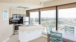 A modern kitchen with a central island, a dining area with a table and chairs, and large windows offering a city view. - Ocean Front resort next to Myrtle Beach Sky Wheel! (Myrtle Beach)