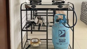 Een keuken met een gasfornuis, een pan, een wok, een gasfles en een wanddecoratie.