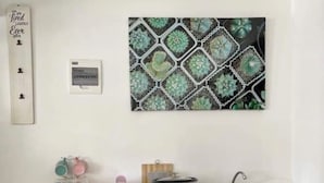 Een keuken met een wit aanrecht, een slowcooker en een spoelbak. Daarboven hangt een decoratieve wandversiering.