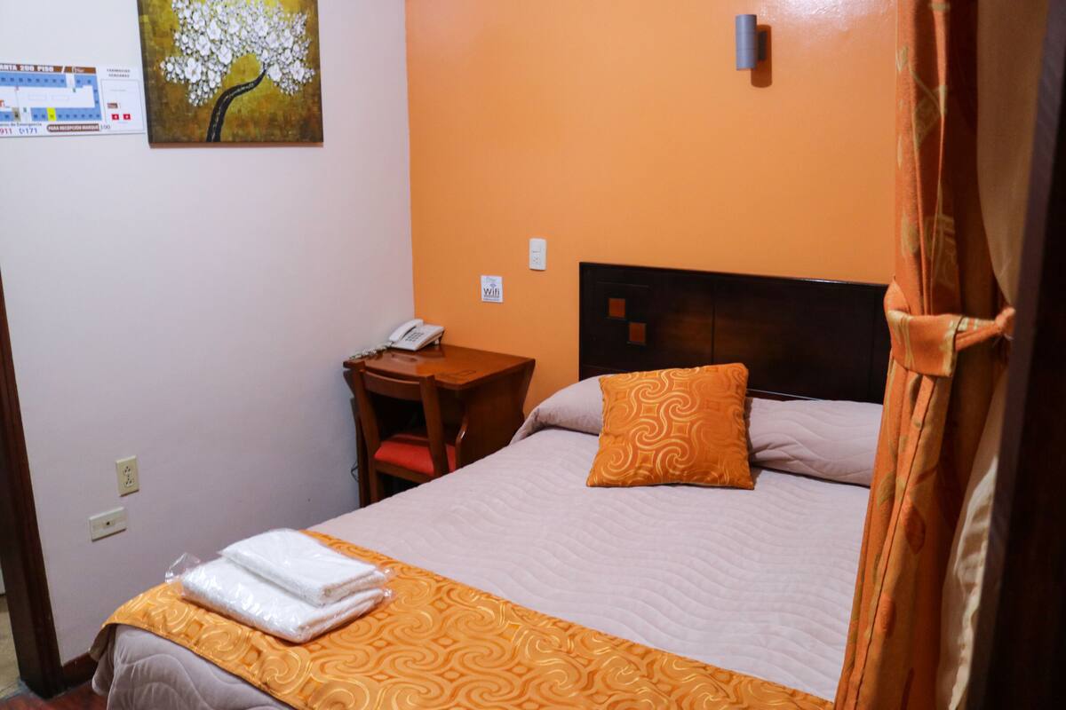 A hotel room with a bed, a desk with a telephone, and a painting on the wall.