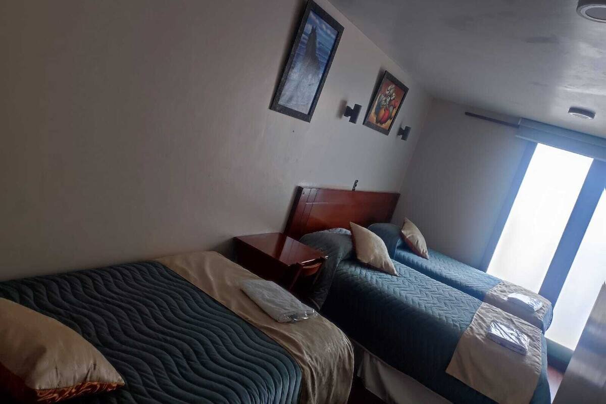 A hotel room with two beds, a wooden headboard, a nightstand, and a window providing natural light.