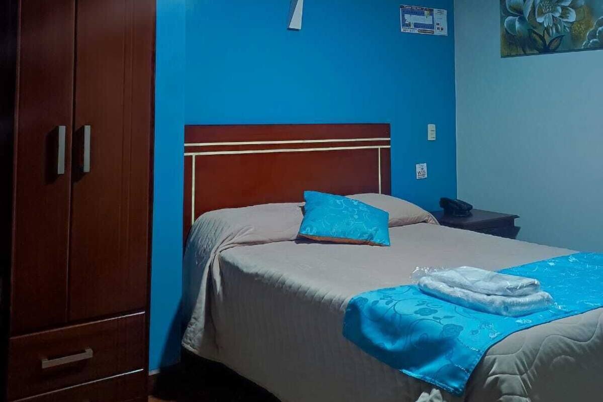 A bedroom with a wooden wardrobe, a bed with blue bedding, and a painting on the wall.