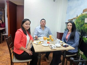 Three people seated at a table with breakfast items, including plates, cups, and a glass of orange juice. - Hotel Villonaco (Loja)