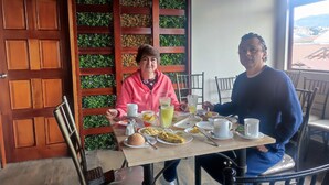 A dining area with wooden furniture, a table set with plates, cups, and a glass of juice. - Hotel Villonaco (Loja)