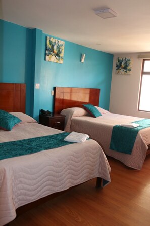 A hotel room with two beds, wooden headboards, teal and white bedding, and artwork on the walls. - Hotel Villonaco (Loja)