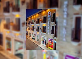 Un edificio de varios pisos con balcones, un letrero que dice 'HOTEL VILLONACO' y locales comerciales que incluyen una farmacia y un bar de tapas.