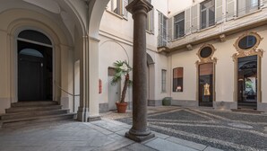 Um pátio com piso de pedra, uma palmeira e um edifício com uma loja à direita.