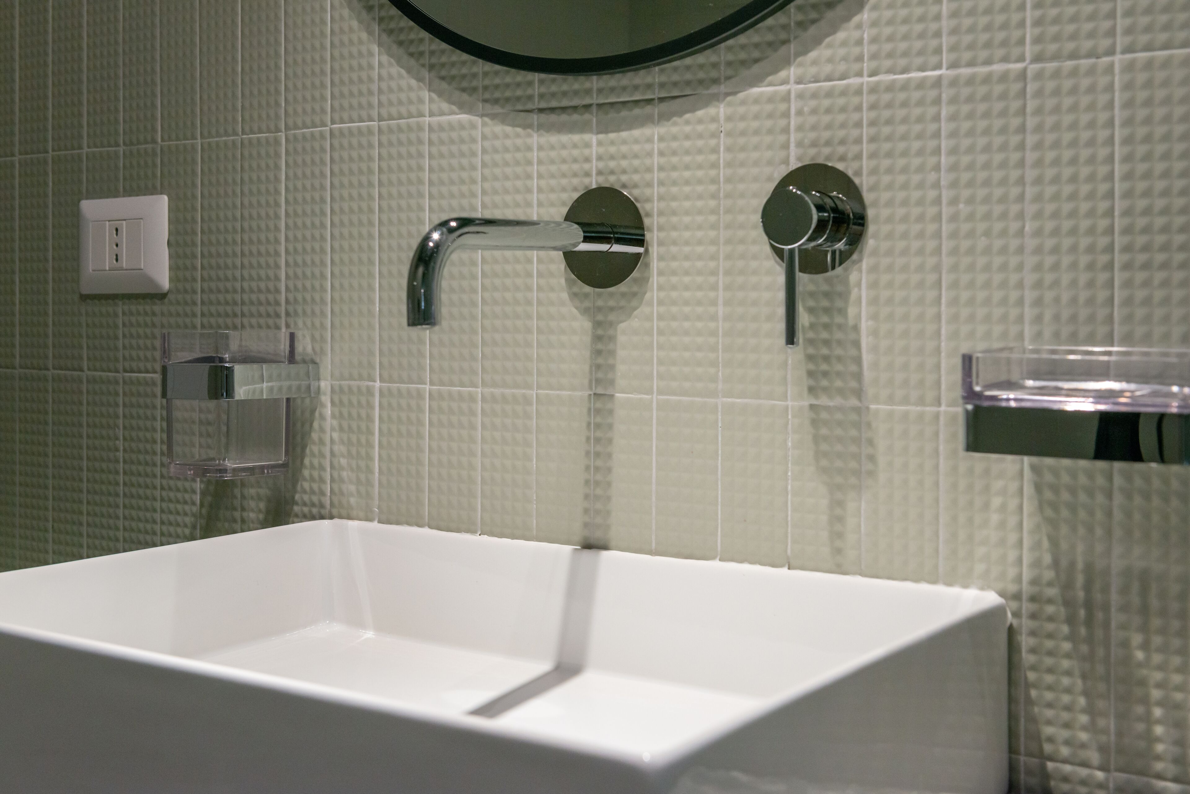 A bathroom with a white sink, a mirror, and a wall-mounted faucet.