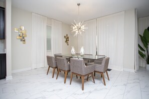 Uma sala de jantar com mesa de vidro, seis cadeiras, lustre moderno e peças decorativas nas paredes.