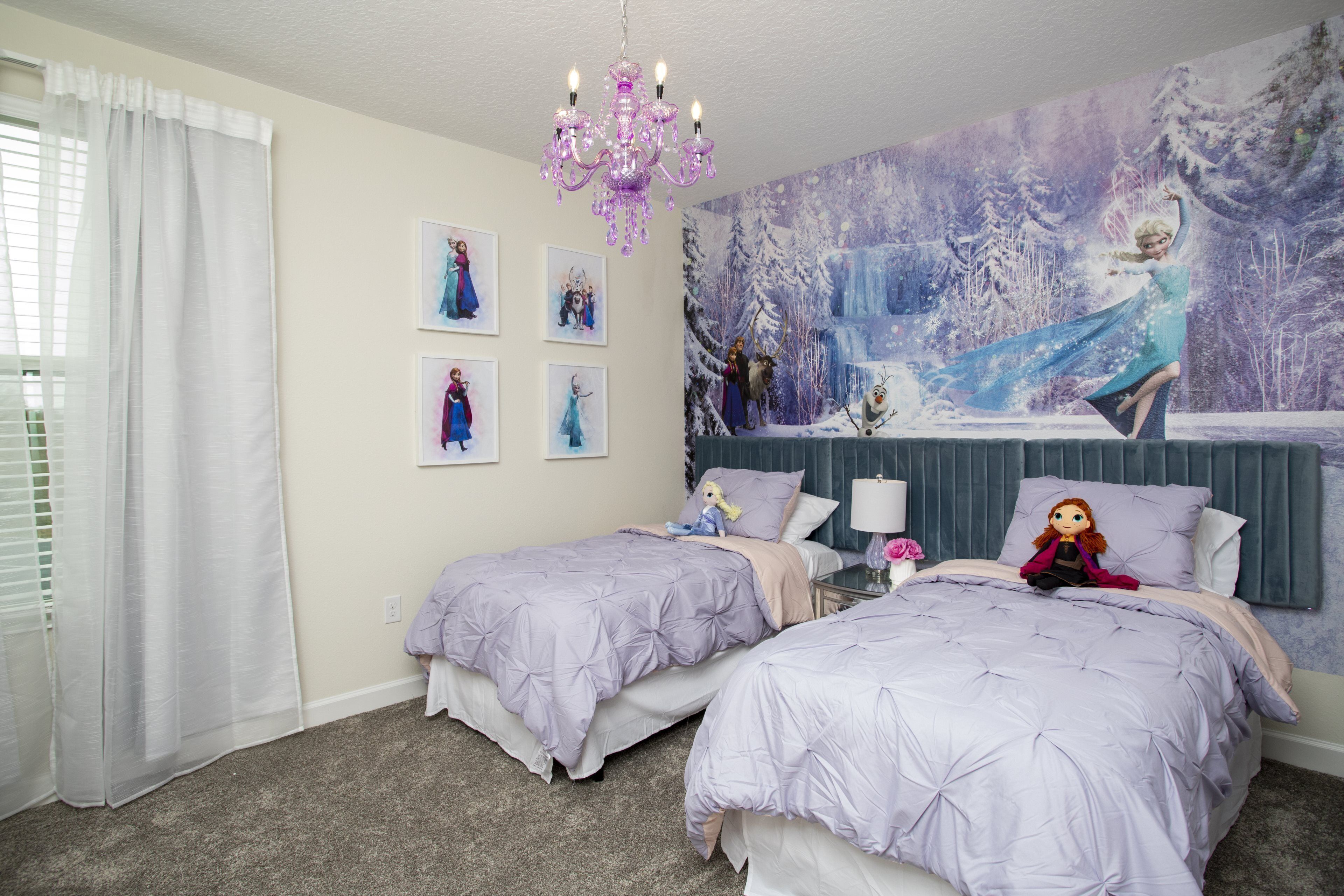 A bedroom with two beds, a chandelier, a large winter-themed mural, and a window with white curtains.